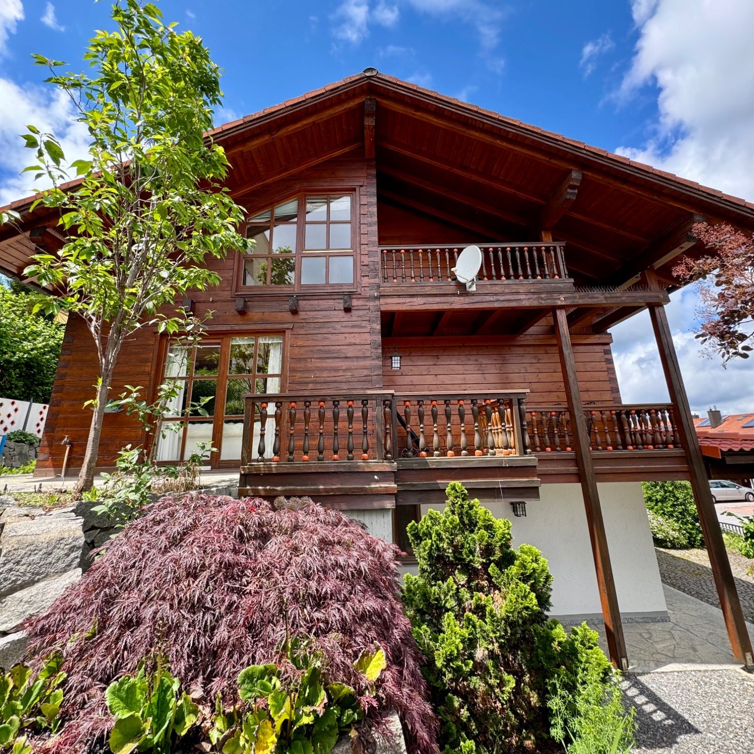 Mehrfamilienhaus mit roter Tür, umgeben von parkenden Autos und grauem Himmel.