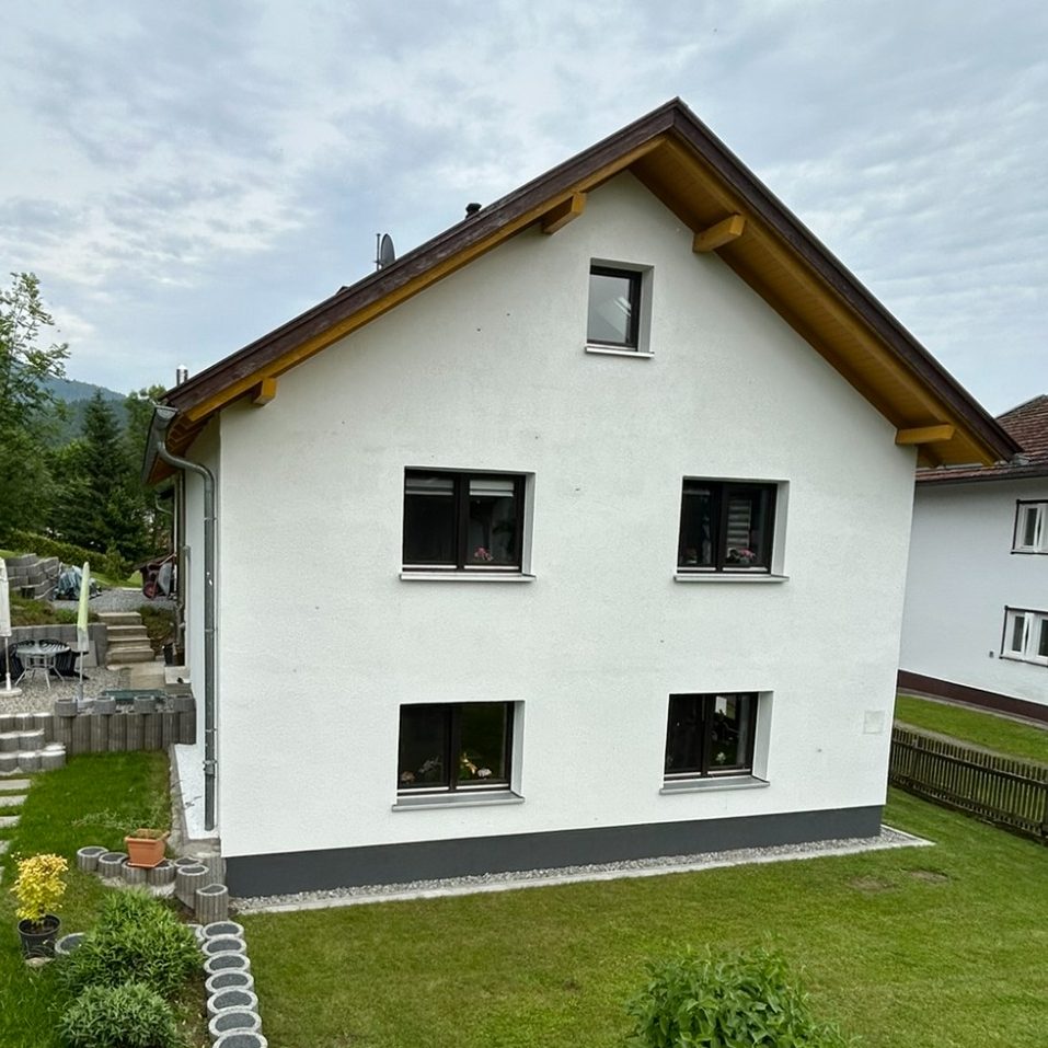 Modernes zweigeschossiges Haus mit verglastem Balkon und Parkplatz.